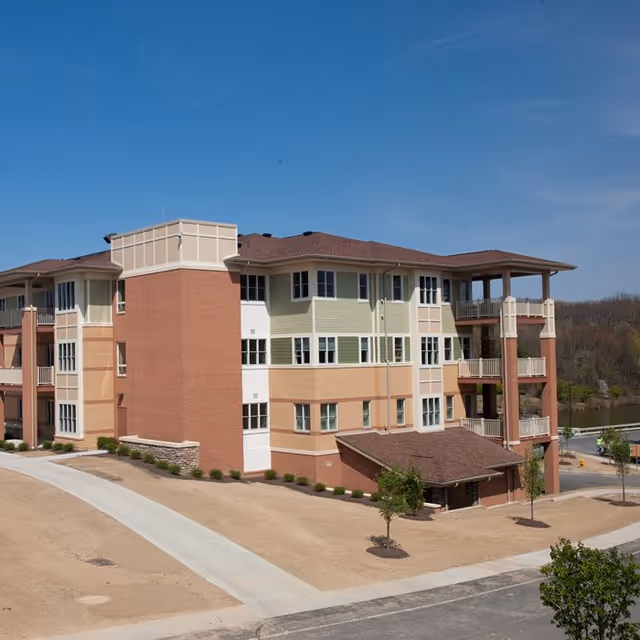 Three-story senior living building with brick and siding exterior, walkways, and blue sky.