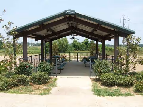 Open-air pavilion with benches and a walking path in a landscaped outdoor space.