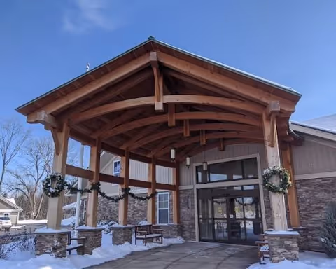 Entrance of a building with a wooden covered porch decorated with wreaths and garlands. Snow is on the ground and benches are placed near the entrance.