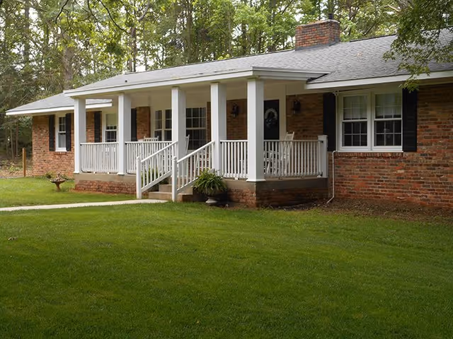 Brick single-story facility with a white, columned front porch, black shutters, and a green lawn.