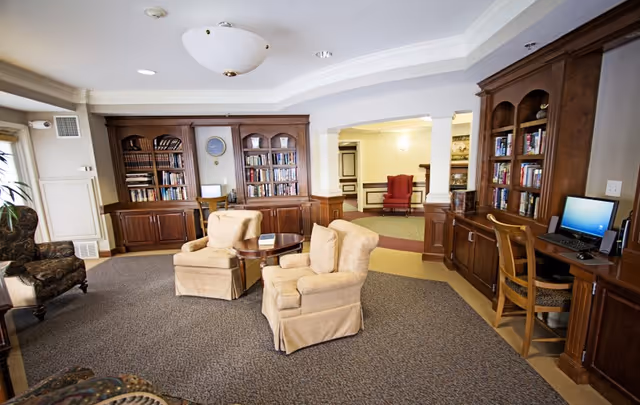 Common area lounge with upholstered armchairs, wooden built-in bookshelves, and a computer workstation.