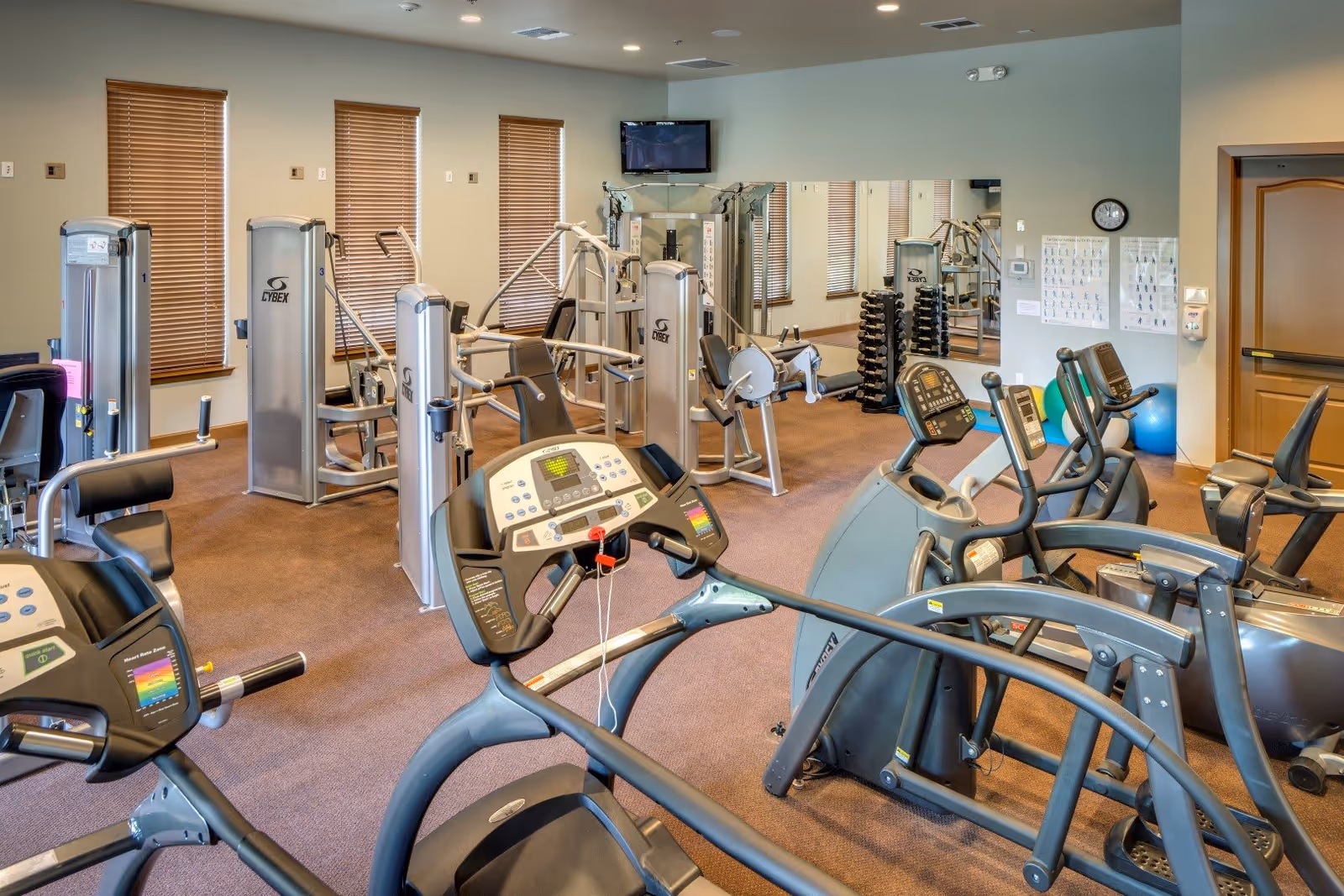 Interior fitness room with treadmills, ellipticals, weight machines, and free weights.