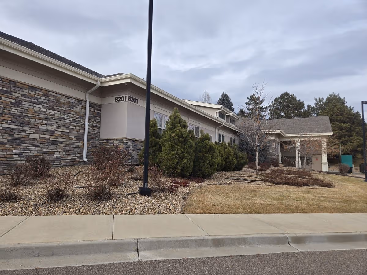 Front exterior of a single-story memory care building with stone siding, landscaping, and address numbers '8201' visible.