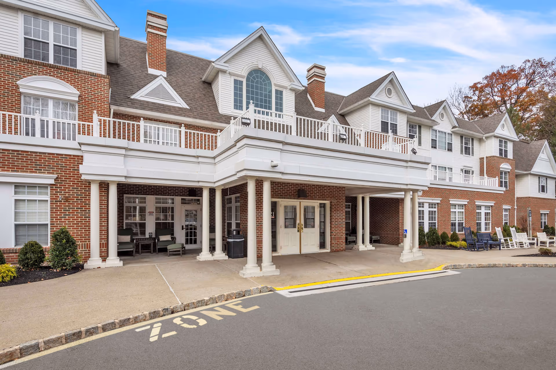 Front entrance of a three-story brick-and-white residential building with a covered porte-cochere, columns, and balconies.
