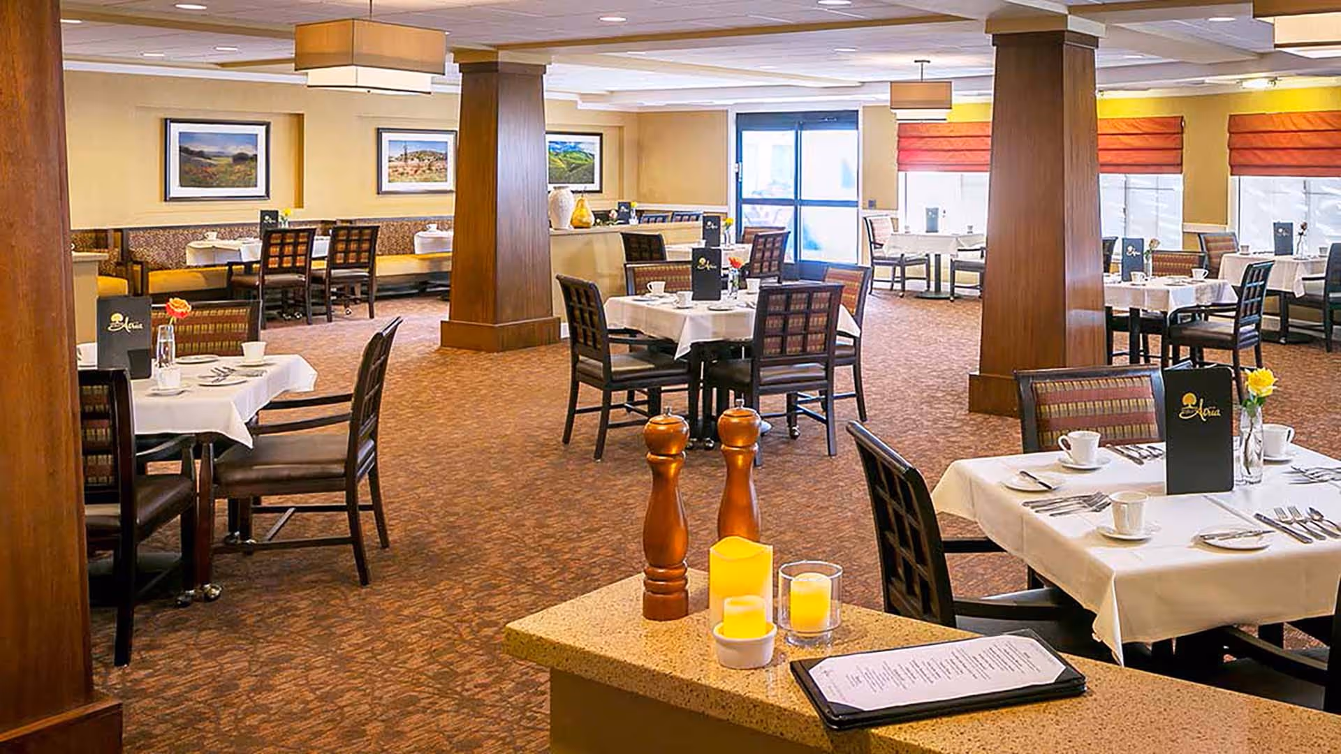 Spacious, well-lit dining room with multiple set tables, chairs, and wooden columns.