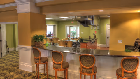 Interior communal dining area with a marble-topped serving counter and bar stools facing an open kitchen and seating area.