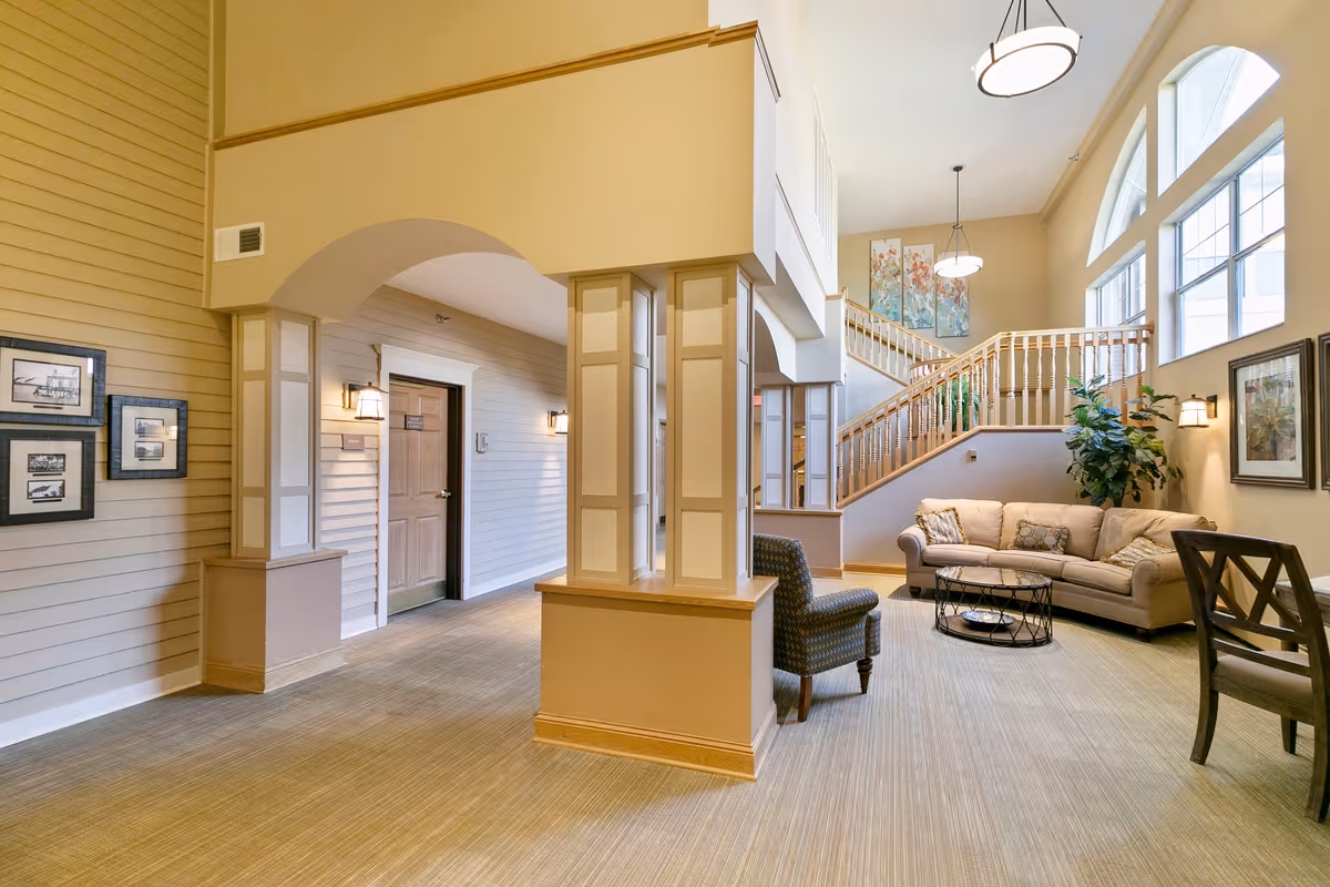 Spacious lounge with sofa, armchairs, a coffee table, and a staircase beneath large arched windows.