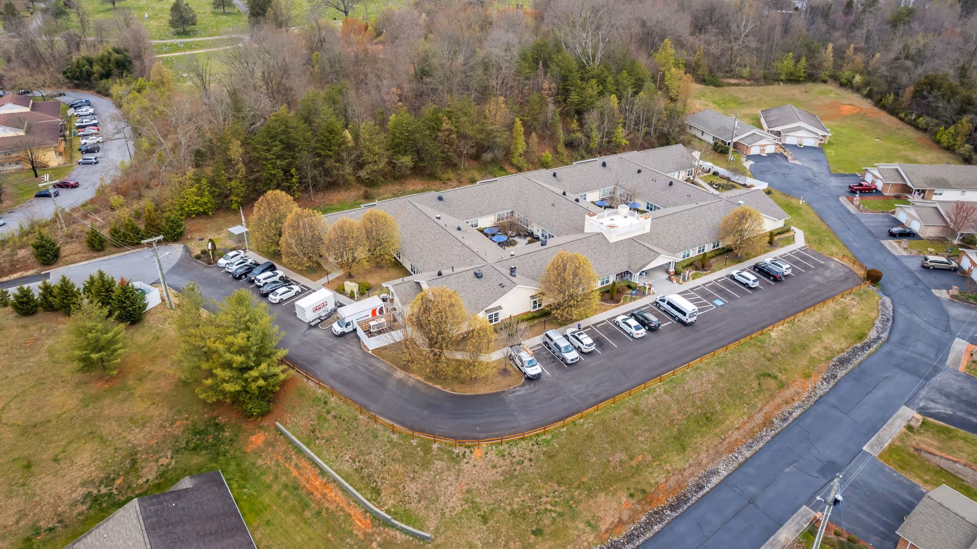 Aerial view of a senior living facility named American House Lebanon, showing a large single-story building with a parking lot filled with cars and surrounded by trees and greenery.