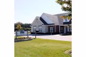 Front exterior of a single-story brick and siding senior living facility with a manicured lawn and entrance sign.