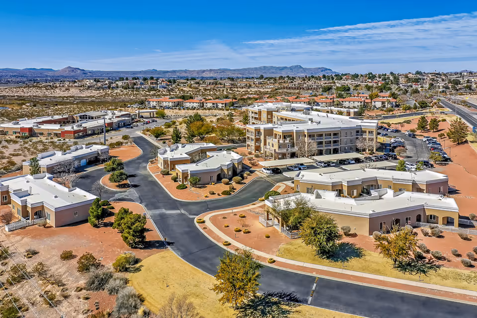 Aerial view of the Solstice Senior Living at Las Cruces campus with multiple low-rise buildings, parking areas, roads, and surrounding desert landscape.