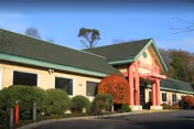 Exterior view of Kin On facility with pink entry arches, green roof, and manicured bushes.