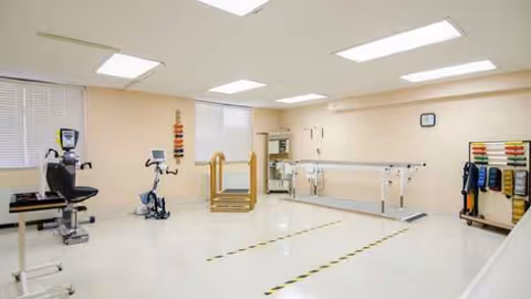 Interior rehabilitation gym in a senior living facility with exercise equipment and parallel bars.