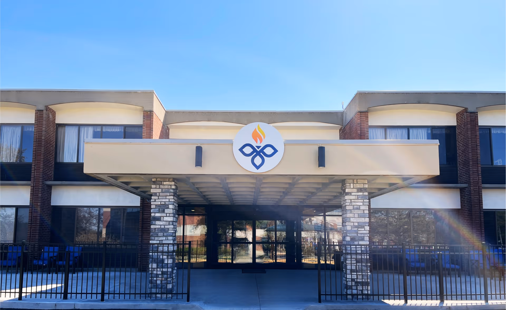 Front entrance of a two-story senior living facility with a covered driveway, stone columns, and a circular emblem above the doors.