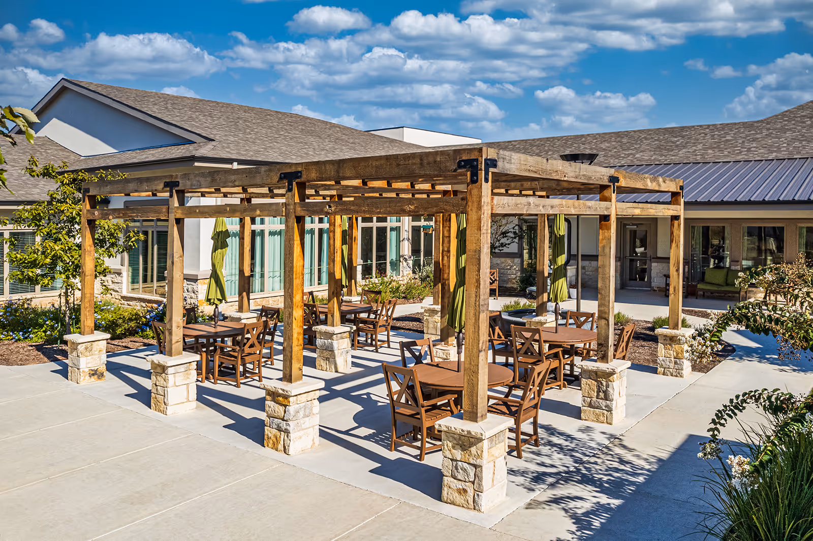 Outdoor courtyard with a wooden pergola and multiple tables and chairs on a paved patio in front of the building.