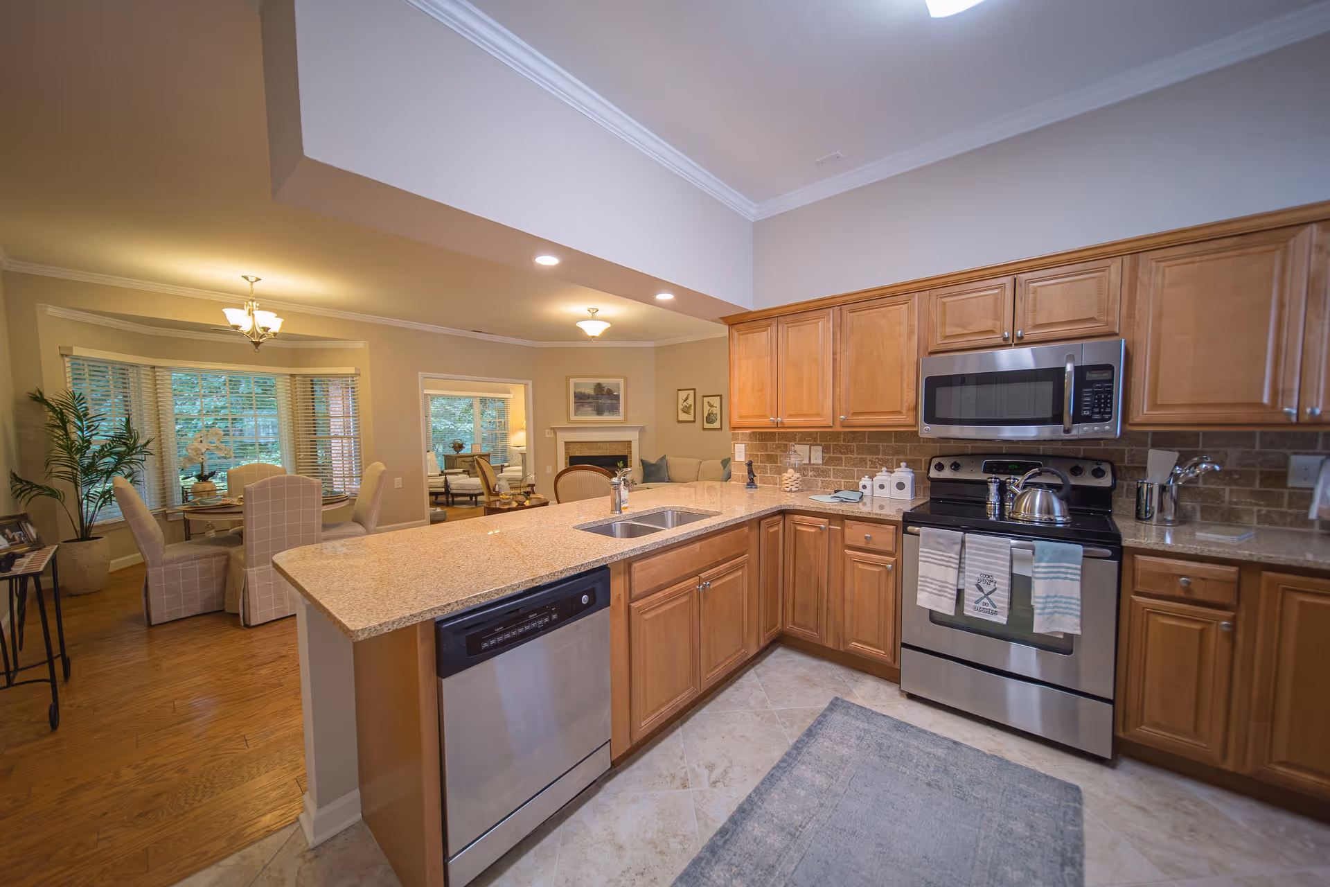 Open-concept kitchen with a large island, stainless steel appliances, wooden cabinets, and a view into the adjacent dining and living area.