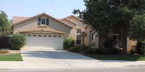 Beige assisted living facility with a two-car garage and manicured lawn.