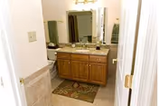 Bathroom with a wooden vanity topped by a granite countertop and mirror, towels, and a tiled floor with a decorative rug.
