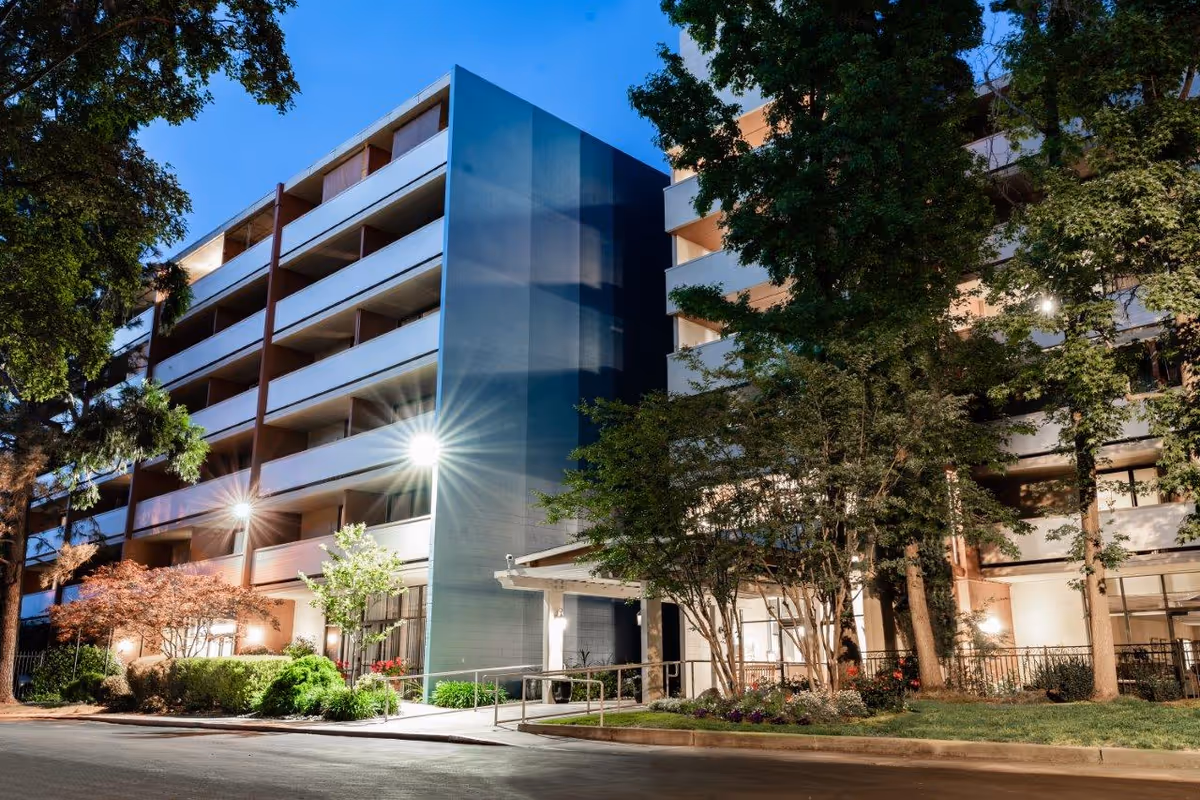 Eskaton Land Park exterior of a modern multi-story senior living building at dusk.