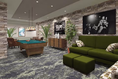 A stylish interior common area featuring a green sectional sofa with patterned pillows, two matching ottomans, a pool table with balls and cues, stone accent walls with black and white framed photographs, potted plants, and modern lighting fixtures.