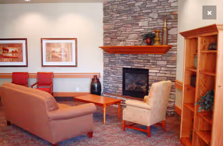 Cozy communal lounge with a sofa, armchairs, coffee table, stone fireplace and wooden shelving.