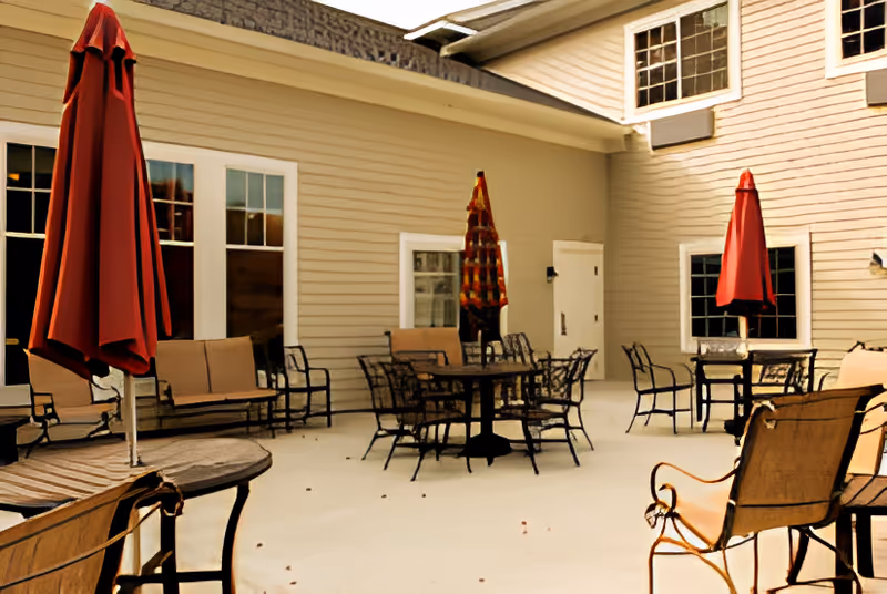 Outdoor courtyard patio with multiple metal tables and chairs and red closed umbrellas beside a beige building.