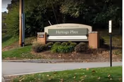 Outdoor sign reading Heritage Place with brick posts and surrounding shrubs at facility entrance.