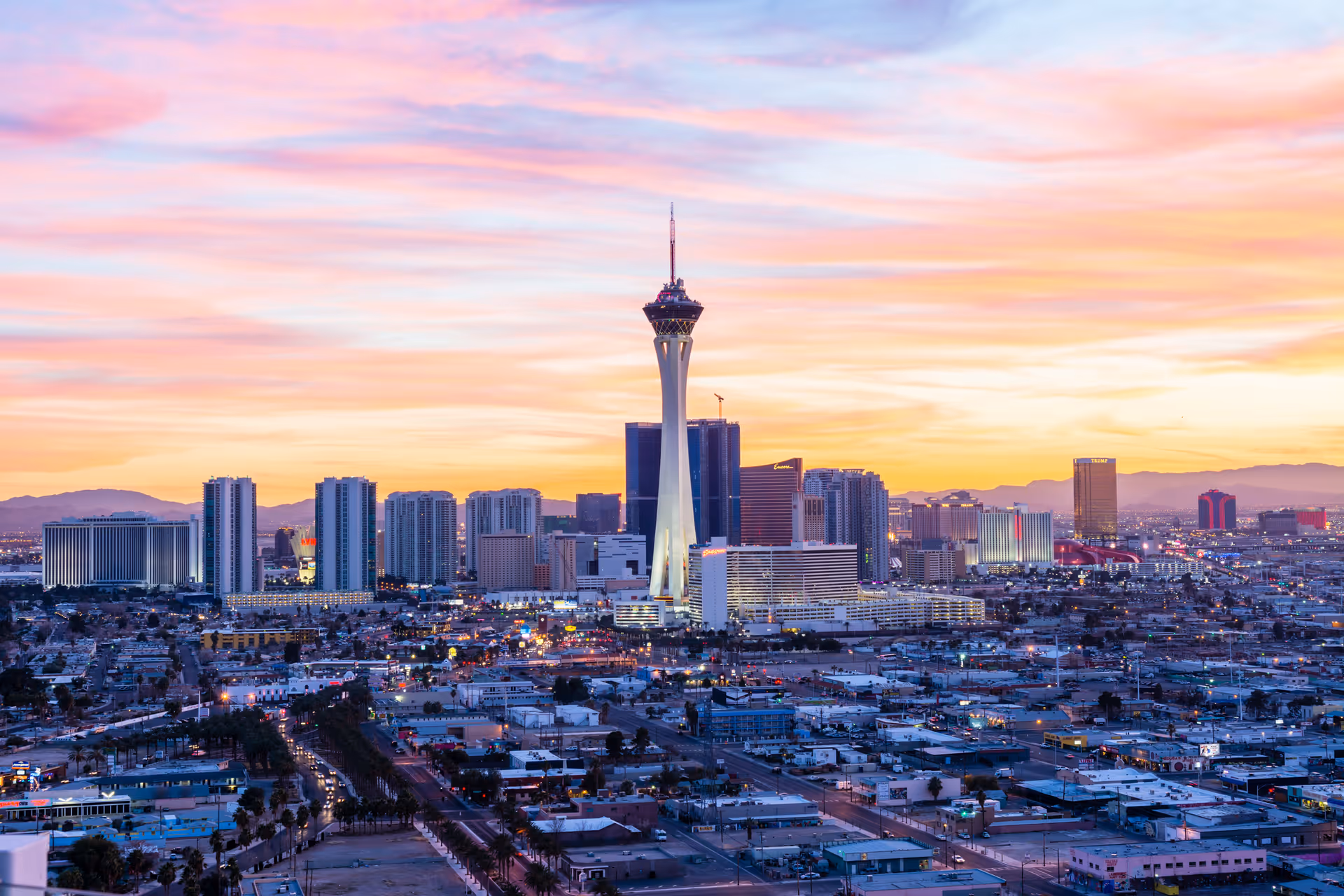 Panoramic city skyline at sunset featuring a tall observation tower and surrounding high-rise buildings.