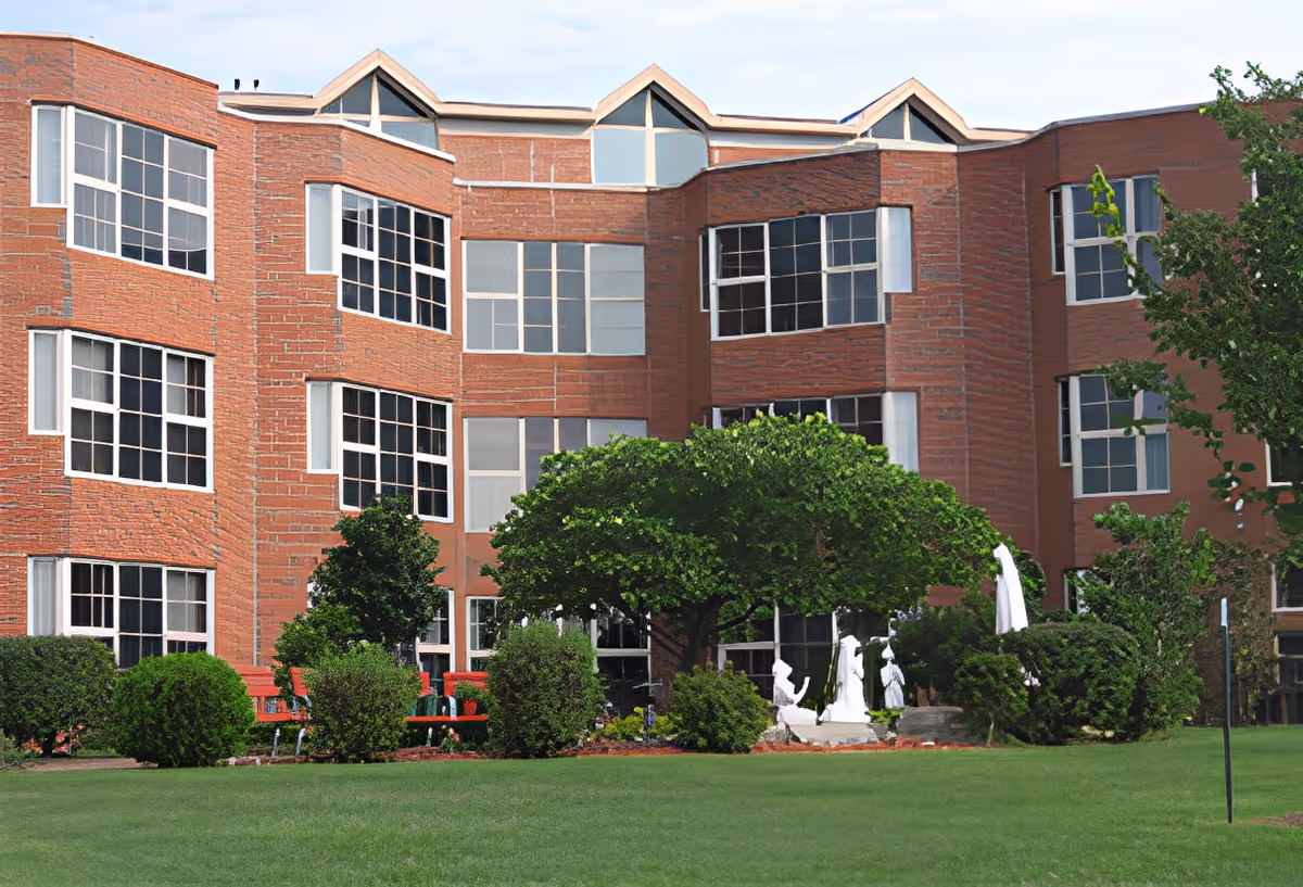 Red-brick multi-story building with large windows, a green lawn, shrubs, and white garden statues.