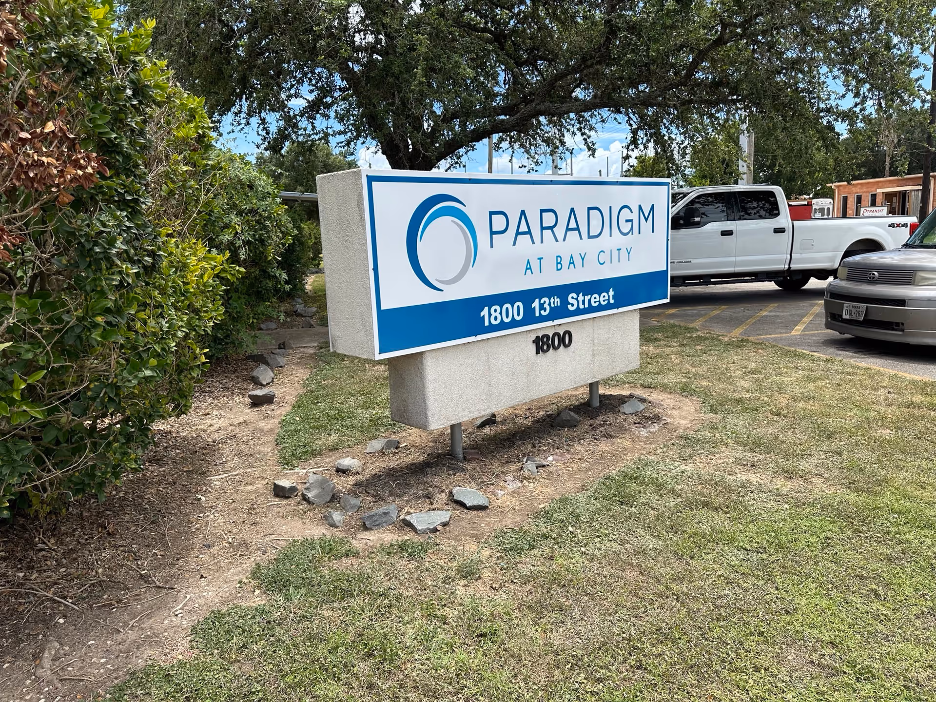 Outdoor sign reading "Paradigm at Bay City" with the address 1800 13th Street in front of a parking area and landscaping.