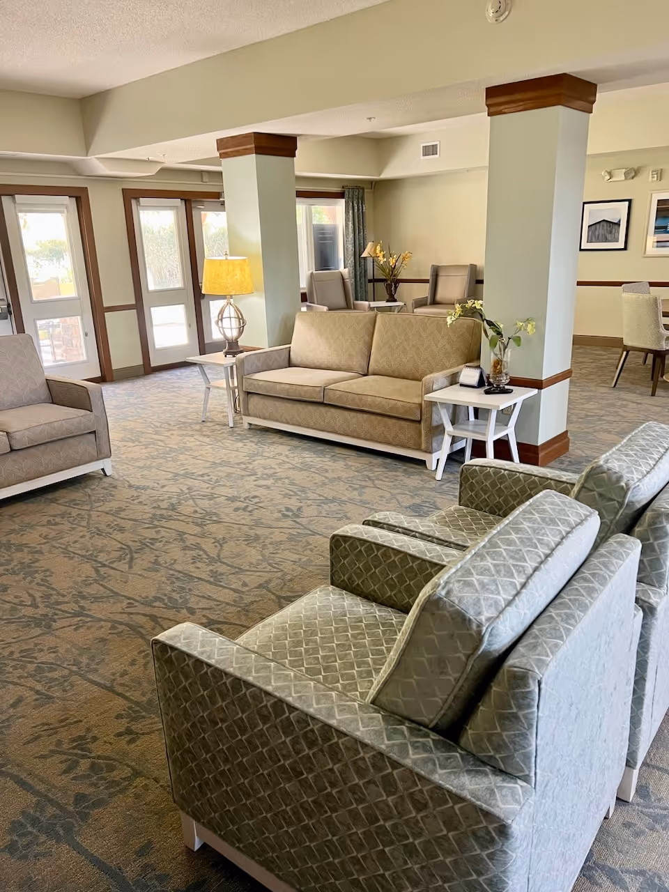 A bright common seating area with sofas, armchairs, side tables, lamps, and decorative columns.