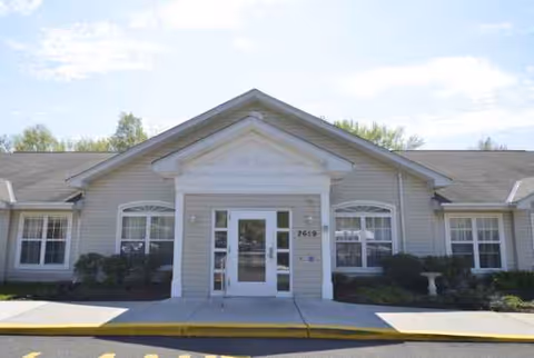 Front view of a single-story senior living facility entrance with glass doors and columns.