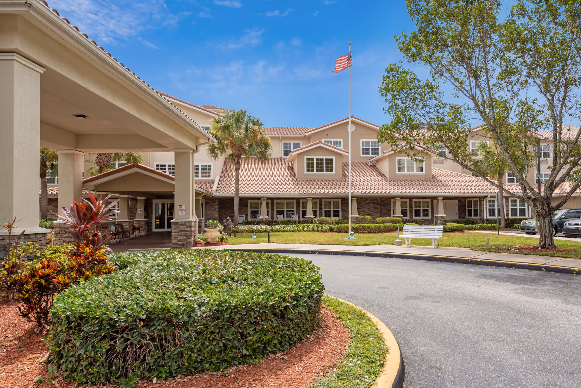 Windward Palms senior living facility exterior with entrance, palm trees, and an American flag.