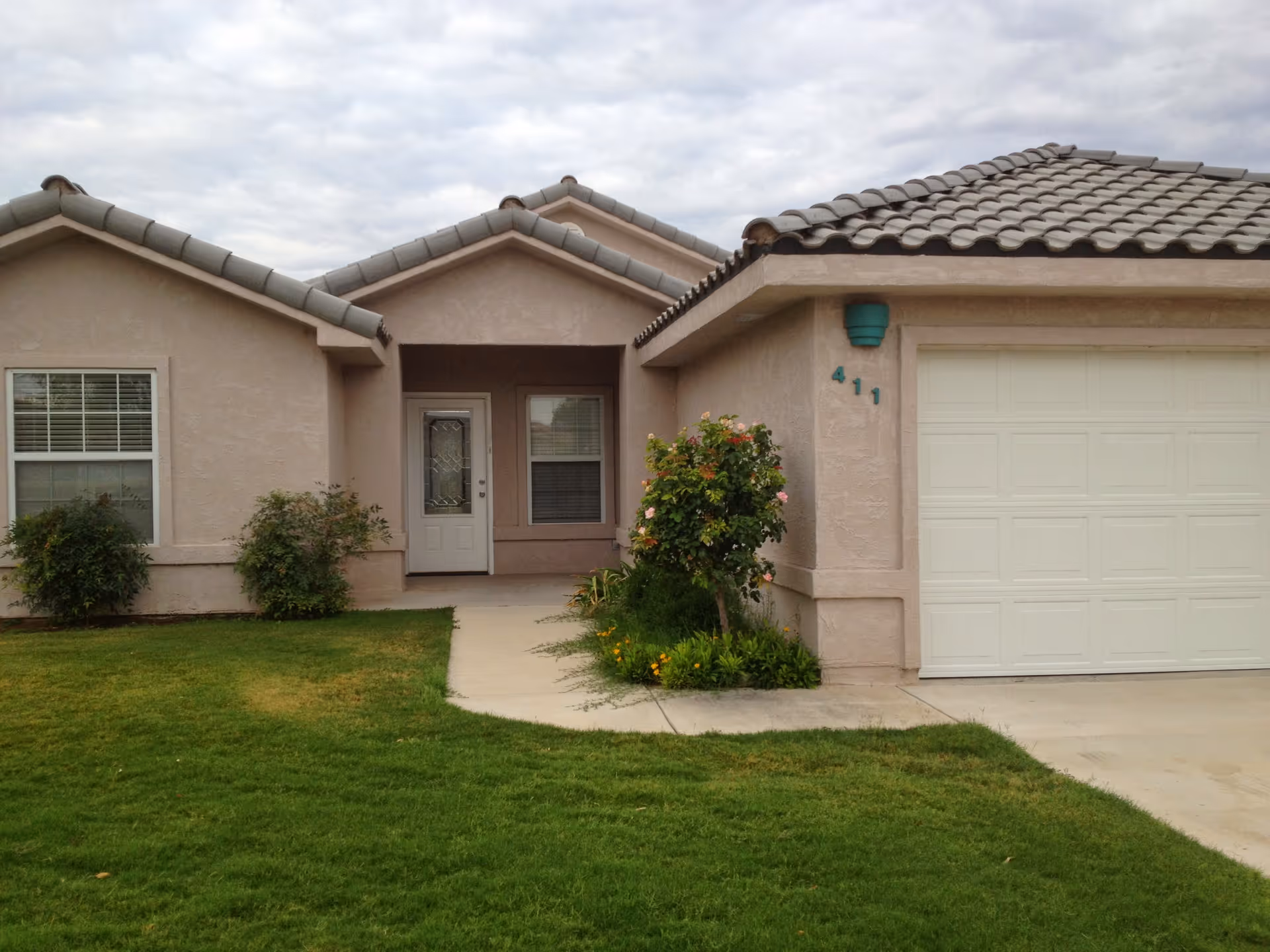 Front exterior of a single-story home with a tiled roof, garage door, entry porch, and a grassy front lawn.