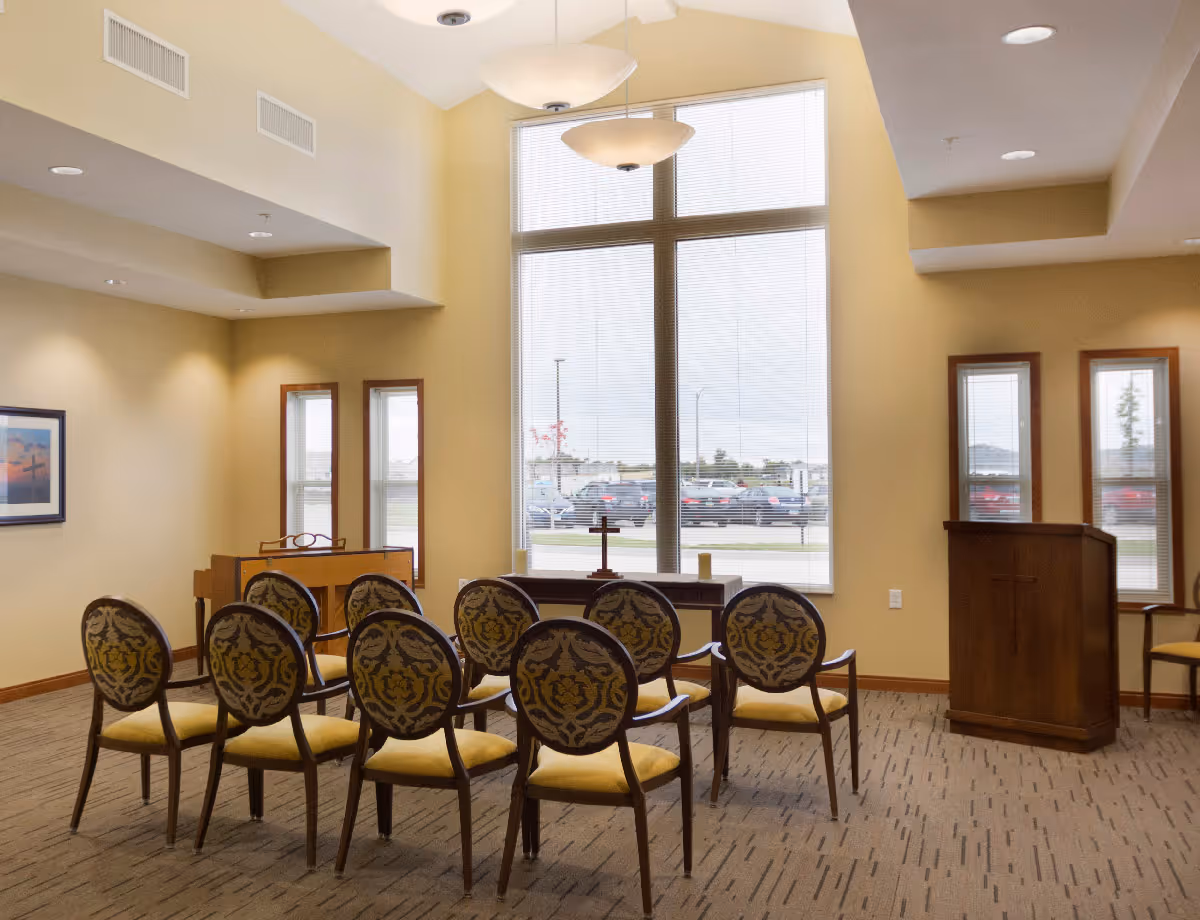 Small chapel or meeting room with rows of patterned chairs facing a large window and a wooden lectern.