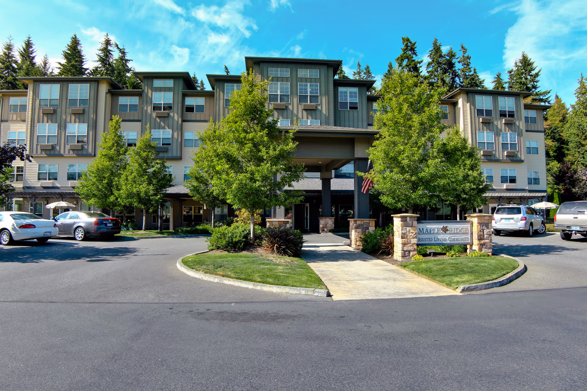 Front exterior view of a multi-story assisted living facility named Maple Ridge by Bonaventure, with a driveway, parked cars, trees, and a sign at the entrance.