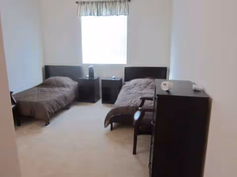 Two twin beds with dark headboards, nightstands, and a dresser in a bright bedroom.