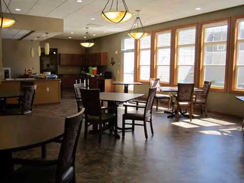 A bright communal dining area with tables, chairs, and large windows.