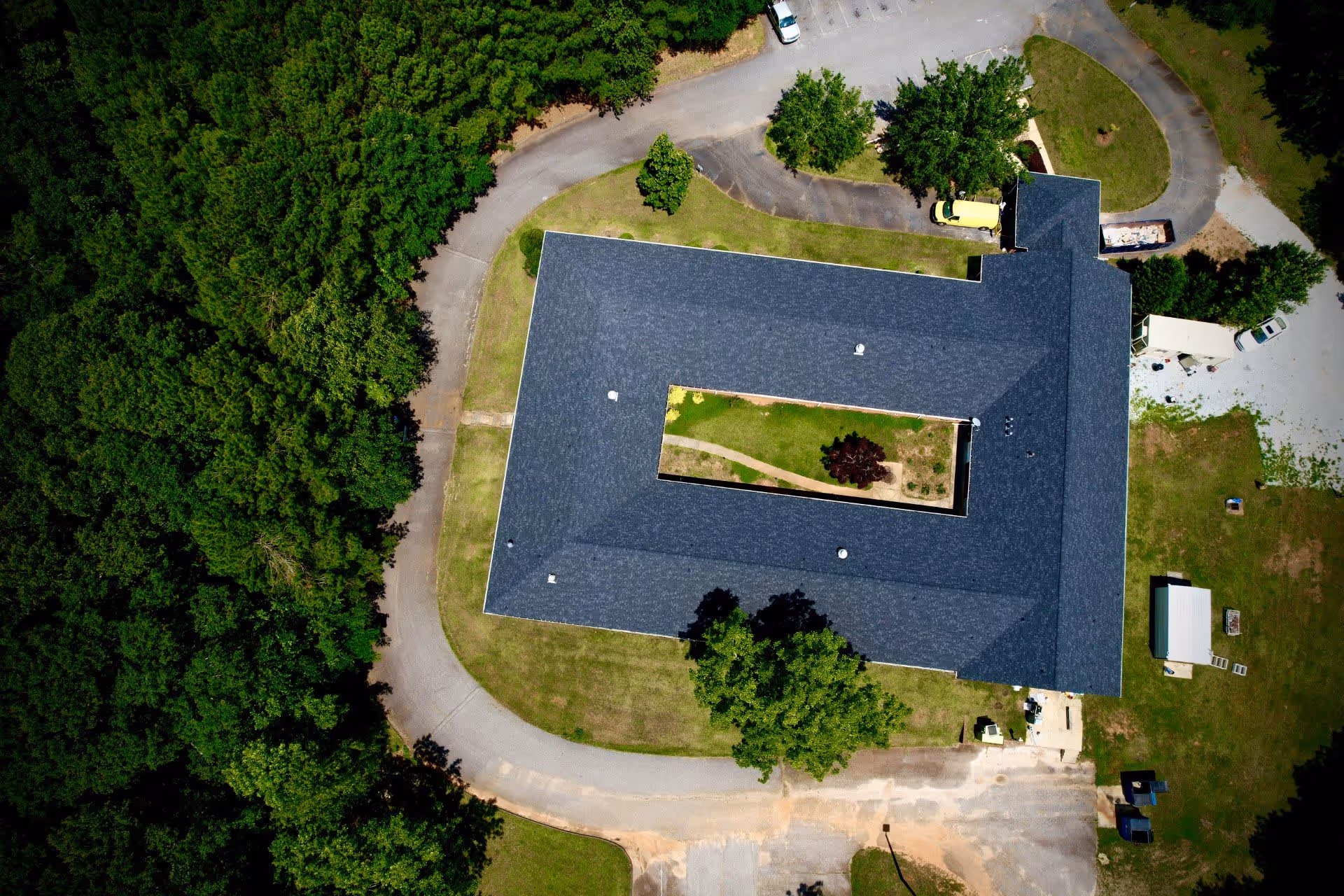 Aerial view of a U-shaped building with a central courtyard, surrounding driveway, parking areas and trees.