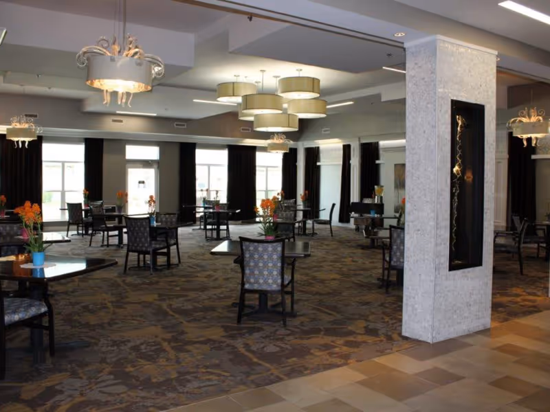 Large, organized dining area with round tables and patterned chairs, modern chandeliers, and large windows.