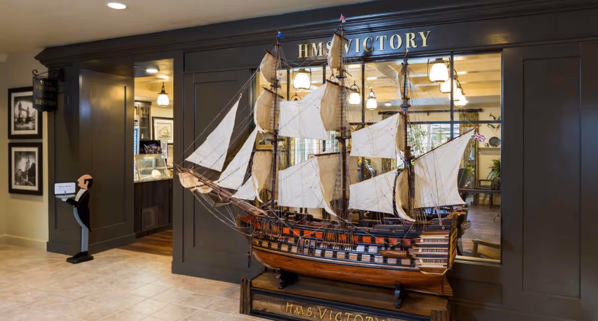A large detailed model of the ship HMS Victory displayed inside a senior living community near the entrance to a bistro area.