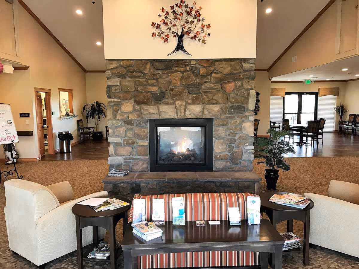 Cozy communal lounge area with a central stone fireplace, upholstered chairs, tables and magazines.