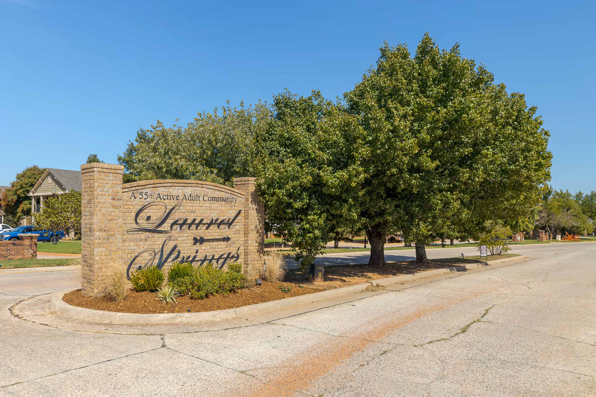 Brick entrance sign for 'Laurel Springs' 55+ active adult community beside a tree-lined street.