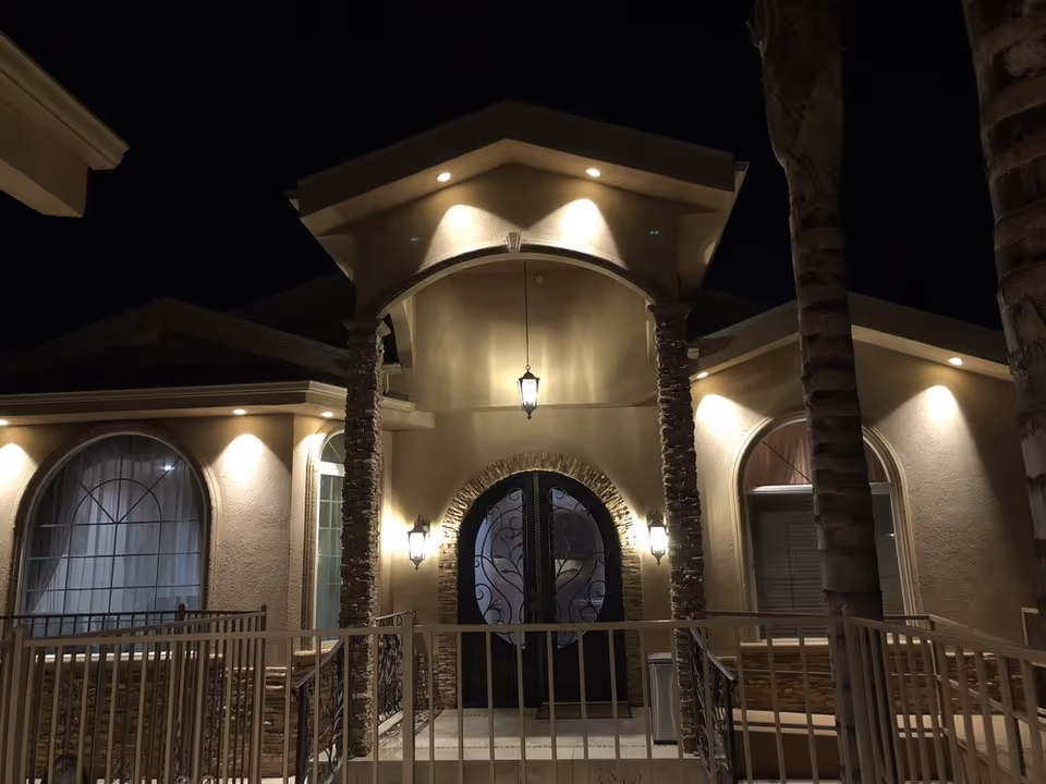 Night view of the front entrance of a senior care facility named Peach Palace Senior Care, featuring a well-lit arched doorway with decorative glass doors, stone pillars, and palm trees on either side.