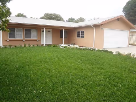 A single-story peach-colored house with a manicured lawn and a white garage door.