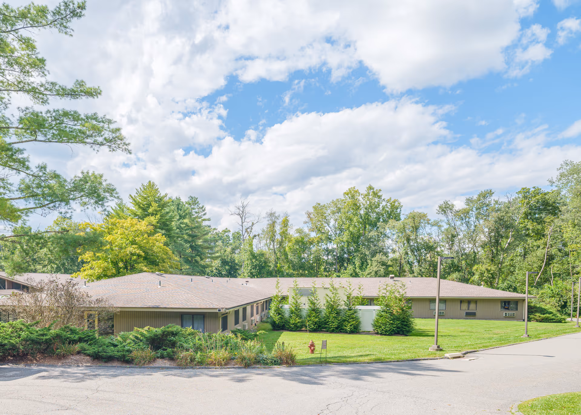 Low single-story building surrounded by lawn and trees under a partly cloudy blue sky.