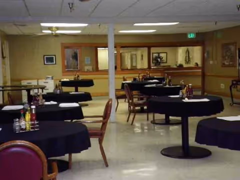 Empty retirement center dining room with round tables covered in black tablecloths.