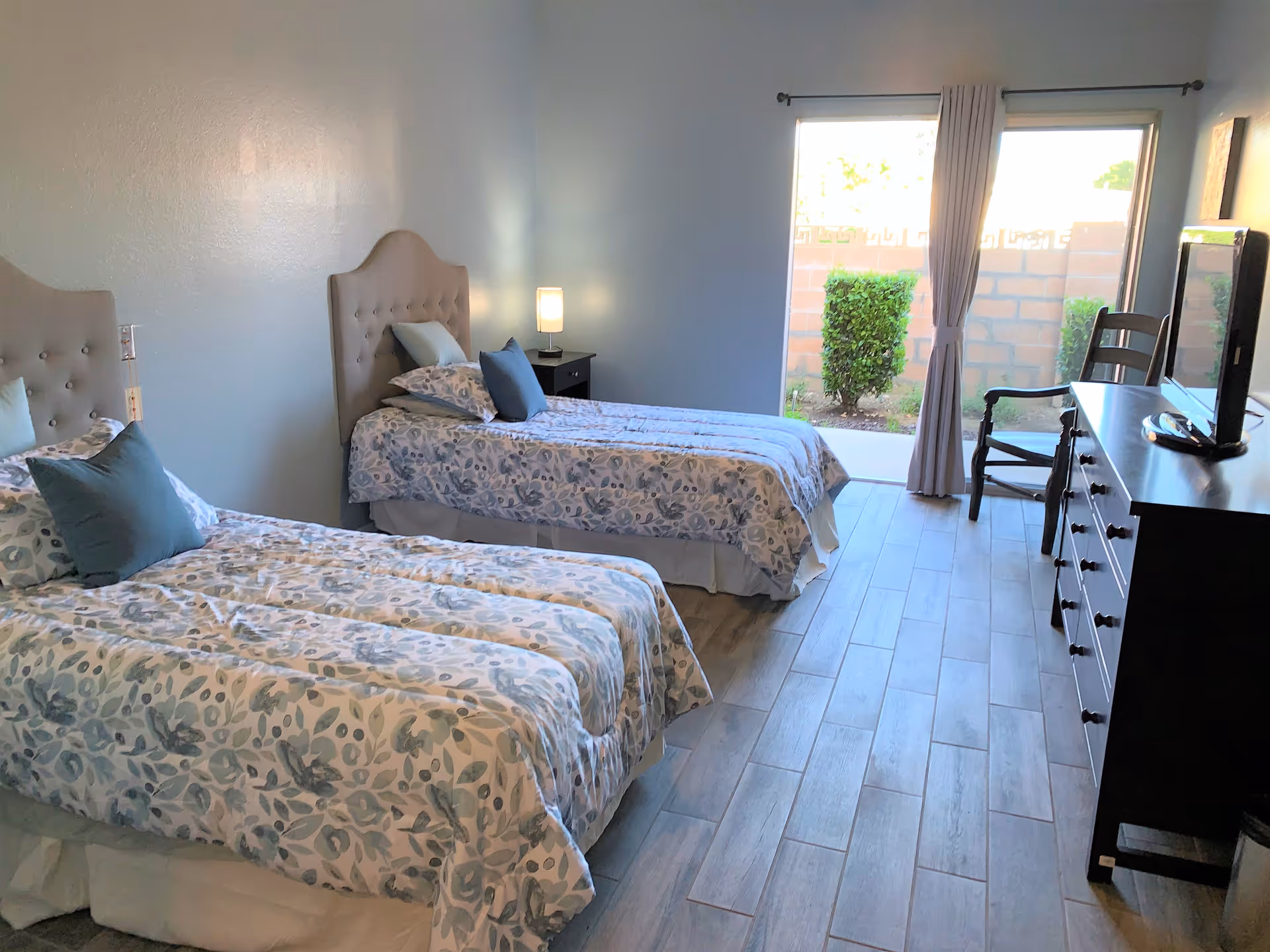 Two twin beds with matching blue floral quilts in a bright senior living bedroom.