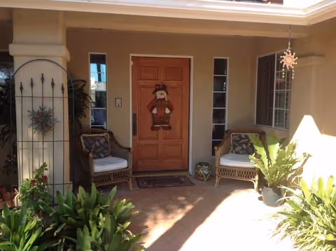 Front porch of Valle Del Sol with wooden door, wicker chairs, and potted plants.