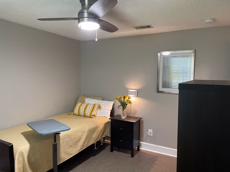 A small, neutral-toned bedroom with a single bed and nightstand.