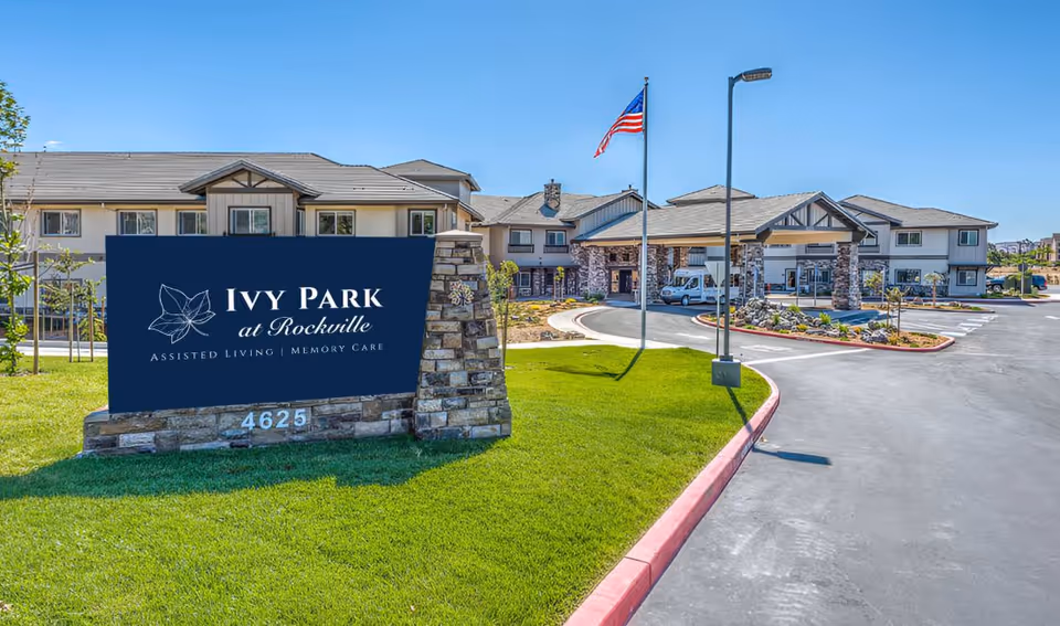 Exterior view of Ivy Park at Rockville with sign, flag, and parking area.